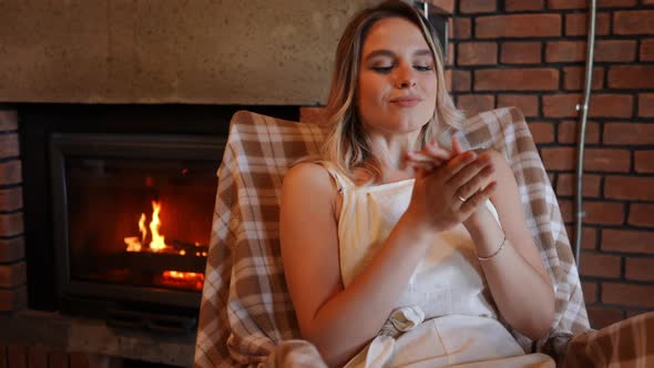 Gorgeous Slim Young Woman Rubbing Hands Looking Away Enjoying Tranquility Indoors with Flame Burning alt