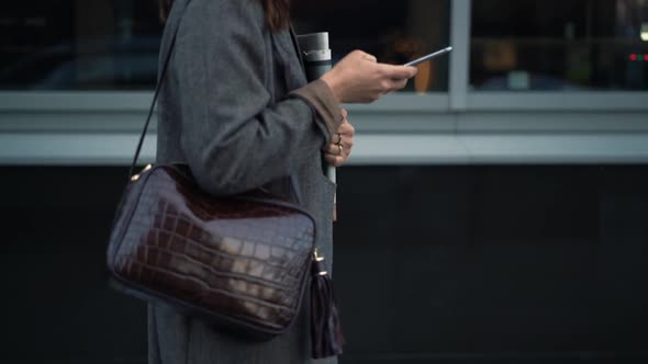 Gimbal Shot of Woman Walking with Newspapers and Typing in the Phone