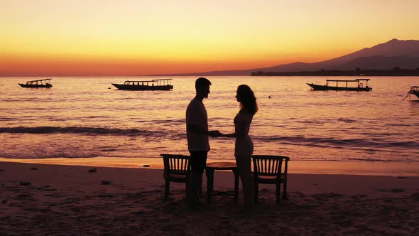 Young couple talking to each other in front of magical lagoon with orange colors of twilight reflect alt