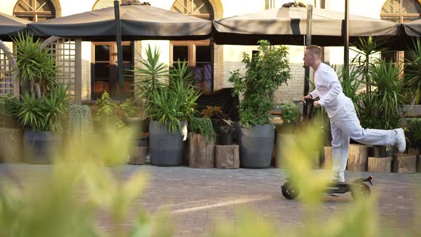 Wide Shot Side View Positive Caucasian Man Riding Escooter in Slow Motion From Right to Left at alt