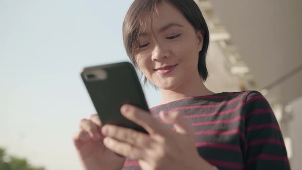 Happy asian woman walks down the city street and use smartphone