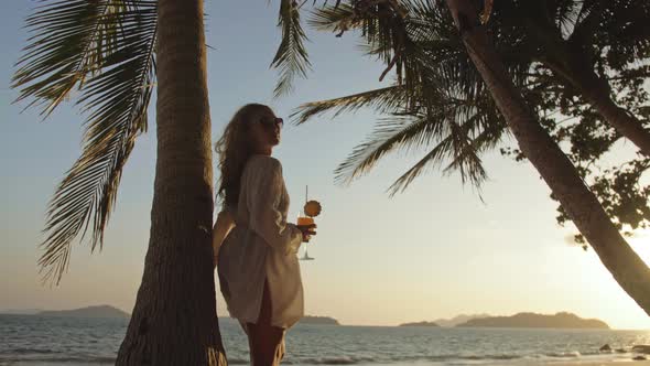 Woman Drinking Pineapple Cocktail Pina Colada Near Palm Tree in White Shirt Sunglasses alt