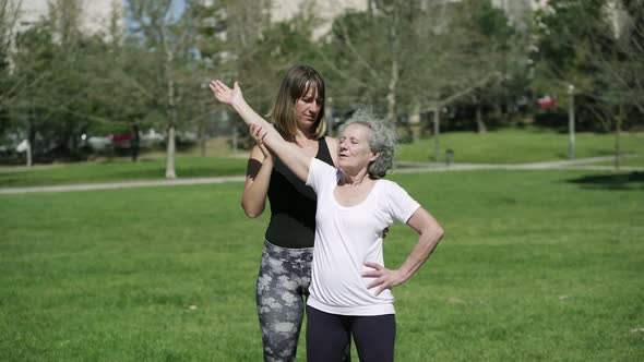 Young Trainer Helping Senior Lady To Stretch Core Muscles alt