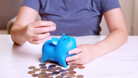 Woman makes savings puts money in a piggy bank. Woman is putting coins into piggy bank. alt