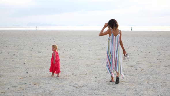 Mom with Two Daughters Walks Along the Beach at Sunset