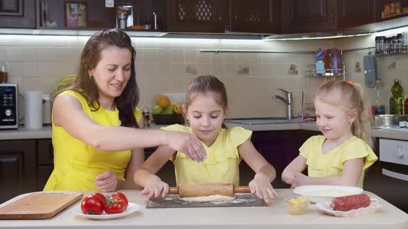 Mom and Children Cook in the Kitchen. Little Girl Smooths Pizza Dough. Mom Helps Children Cook Pizza alt