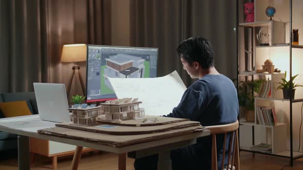 Male Engineer Opening And Looking At The Blueprint While Designing House On A Desktop At Home alt