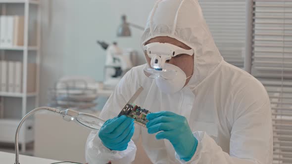 Engineer in Coveralls Examining Printed Circuit Board in Lab alt