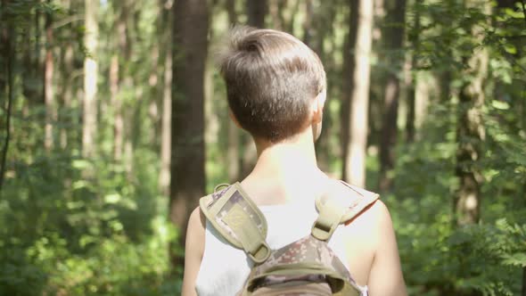 Funny Boy with a Backpack Walks Through the Forest Back View
