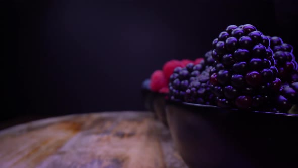 Blackberries, blueberries, raspberries in black bowls, on a black background.