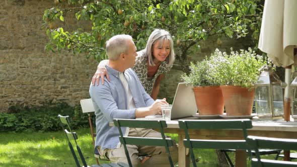 WS, Senior couple at table in garden looking at laptop computer alt
