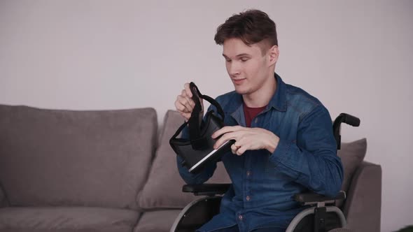 Adult Man in Wheelchair Holding Virtual Reality Helmet in Hands