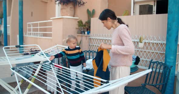 Young Woman with Daughter Baby Girl Hanging Up Wet Laundry Outdoors alt