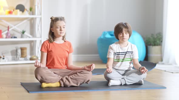 Concentrated Caucasian Girl Sitting on Exercise Mat with Eyes Closed As Boy Repeating Yoga Training alt