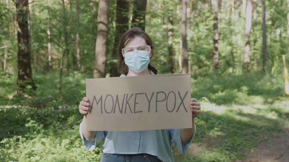 Woman in Glasses Mask with Poster is Worried About Outbreak of Monkeypox alt