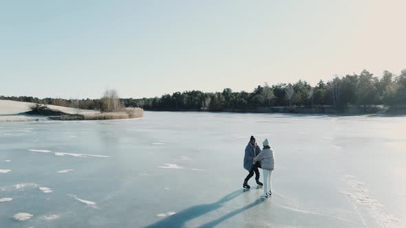Aerial Shot of Couple Skating on a Blue Frozen Lake Holding Hands on a Sunny Day