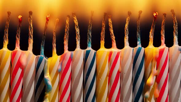 Closeup Set of Colorful Birthday Candles Burning in Timelapse on Black Background alt