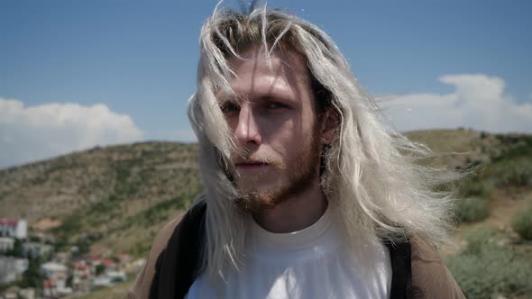 Mysterious Fellow with Long Blond Hair Stands in the Mountains in Windy Weather