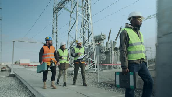 A Team of Energy Engineers, One of Whom Is African and a Woman, Walk Through the Substation.