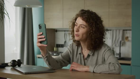 Curly 20s Caucasian Woman Greeting and Talking with Her Friends on a Video Call in Her Apartment alt