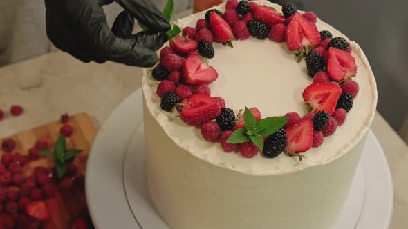 Woman Decorating Delicious Cake with Fresh Berries and Mint Leaf Rotating Table