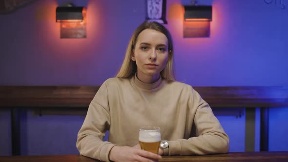 Portrait of a Serious Woman in Pub with Glass of Beer in Hand at Bar Counter