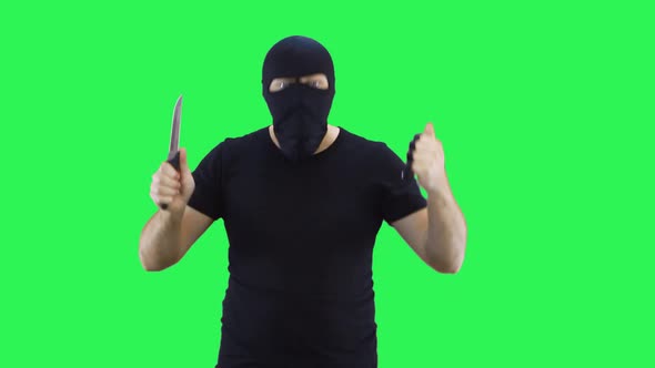 A man in a black mask holds a knife and brass knuckles in his hand