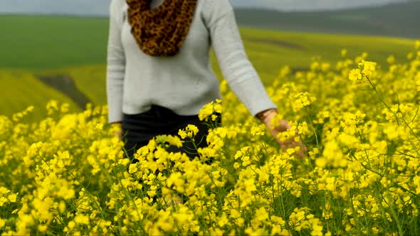 Young woman walking through beautiful yellow canola fields alt