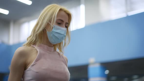 Portrait of Caucasian Young Woman with Dyed Blond Hair in Covid19 Face Mask Running on Treadmill in alt