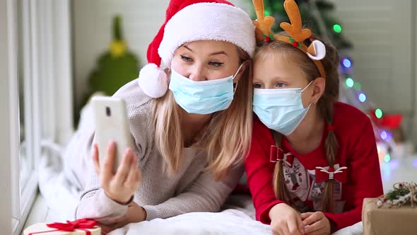 Mom and daughter in medical masks wish a Happy New Year on a mobile phone with family and friends