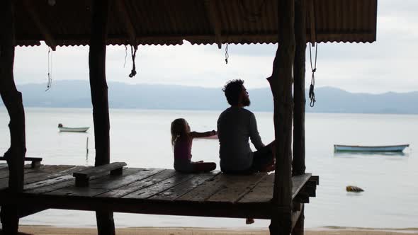 Dad and Daughter are Sitting on the Bridge Near the Sea alt