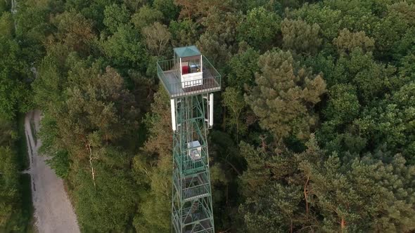 Tall steel forest observation tower and dirt road, fly out aerial drone view alt