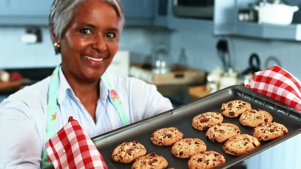 Senior woman holding a tray with homemade cookies in kitchen alt