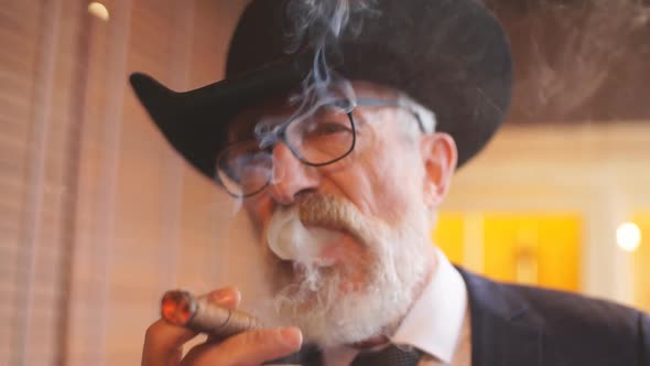 Stylish Old Man Smokes a Cigar and the Smoke Released From the Mouth alt