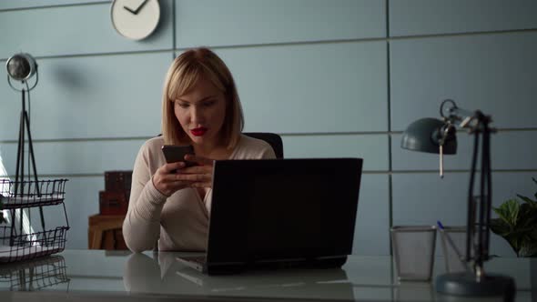 A Close-up Portrait of a Middle-aged Woman with Blond Hair, Sitting in an Office at a Laptop on a alt