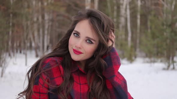 Young Woman with Wavy Hair Standing and Touching Face in Winter Forest