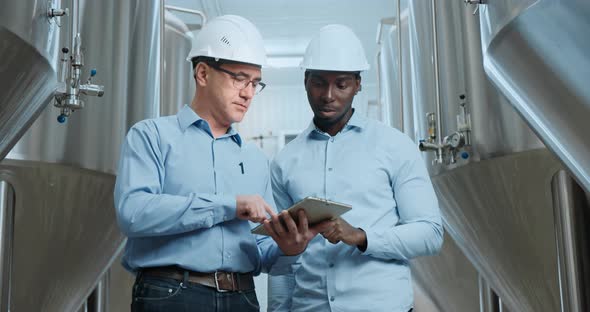 Two Industry Engineers Walk in Factory Use Tablet and Discuss Work alt