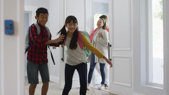 Excited asian son and daughter running through front door, returning home with parents alt