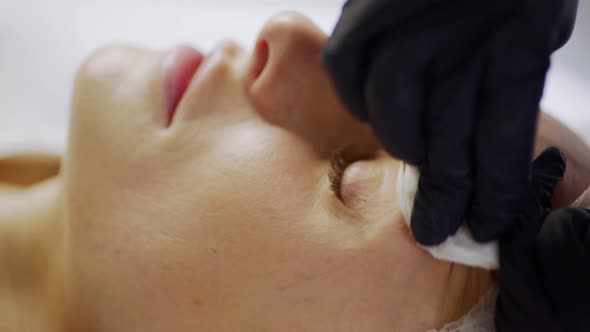 Beautician Cleans Eyebrow of Woman with Cotton Pad in Salon