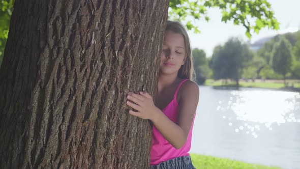 Smiling Teenage Girl Hugging Tree with Eyes Closed at Park alt