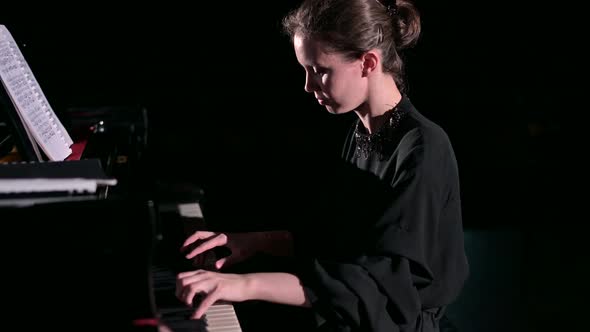 A young woman plays the piano energetically in the spotlight on the stage alt