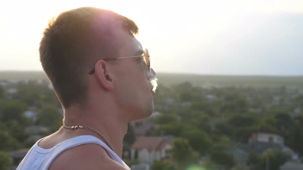 Profile of Handsome Guy in Sunglasses Standing on the Edge of Rooftop and Smoking Cigarette with alt