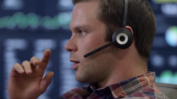 Side view of man talking on headset in front of computer screen. alt