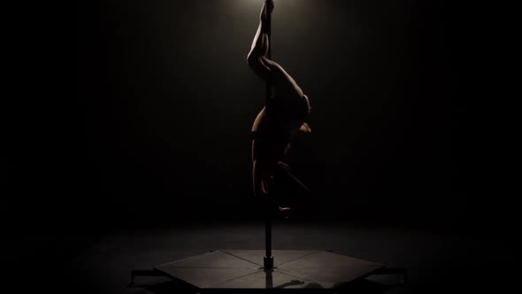 Dancer Spinning on a Pole . Black Background. Slow Motion. Silhouette alt