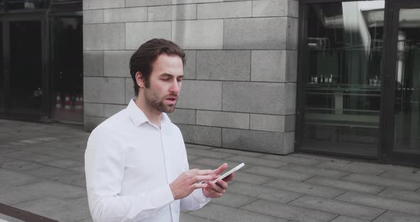 Young Man Texting Messages Cheating on His Smartphone While Walking in Office District alt
