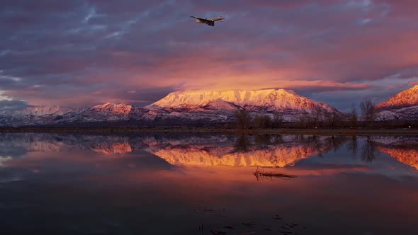 Airplane flying through the sky during colorful sunset with snow capped mountain alt
