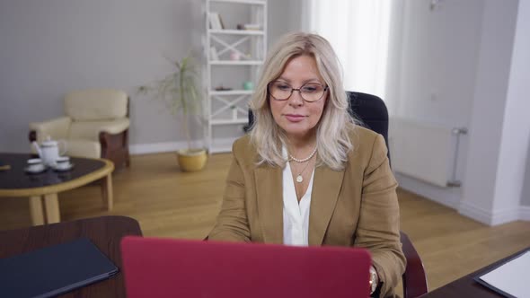 Front View Confident Woman in Eyeglasses Surfing Internet on Laptop and Looking at Camera Smiling alt
