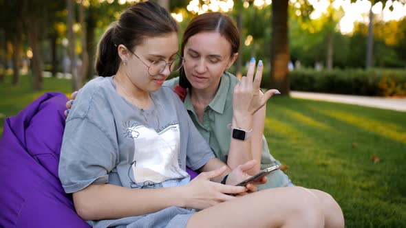 Mom and Her Teenage Daughter are Sitting on Large Colorful Pillows on the Lawn in the Park with a alt