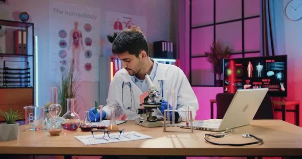 Chemist in Medical Uniform and Gloves Looking through Microscope on Biological Samples alt