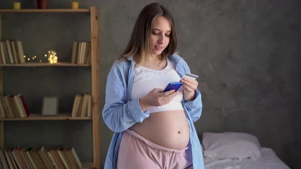 Young Pregnant Woman Shopping on Internet Using Banking App or Service on Smartphone and Credit Card alt